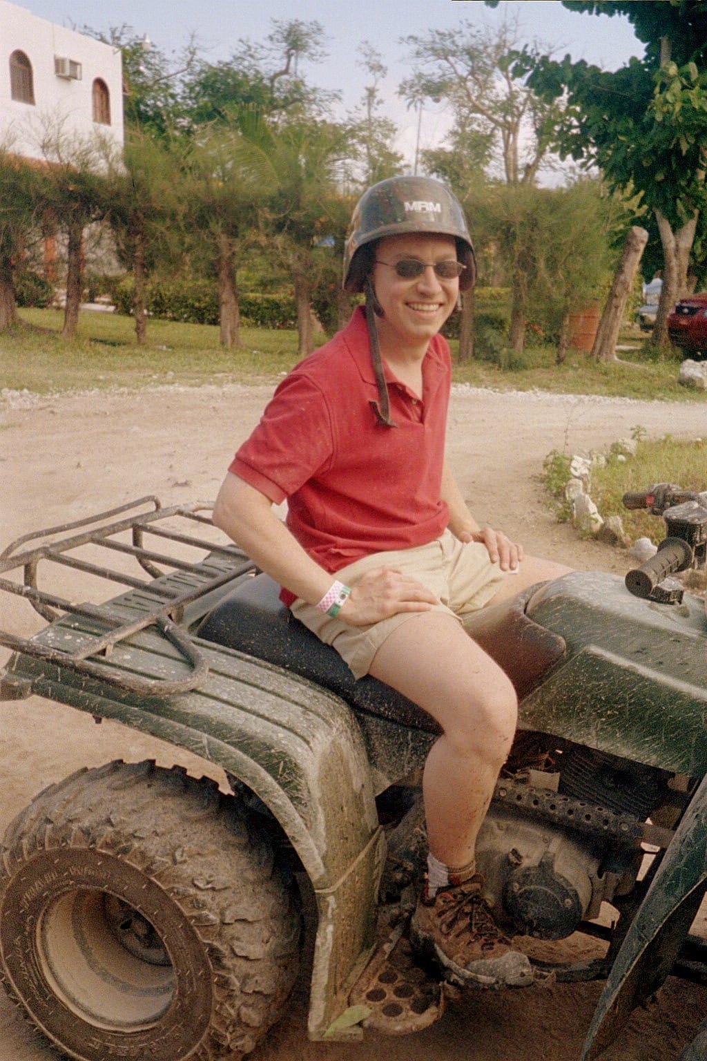 Scott sitting on ATV in Mexico smiling, grimy, and mud covered after his first ATV ride.