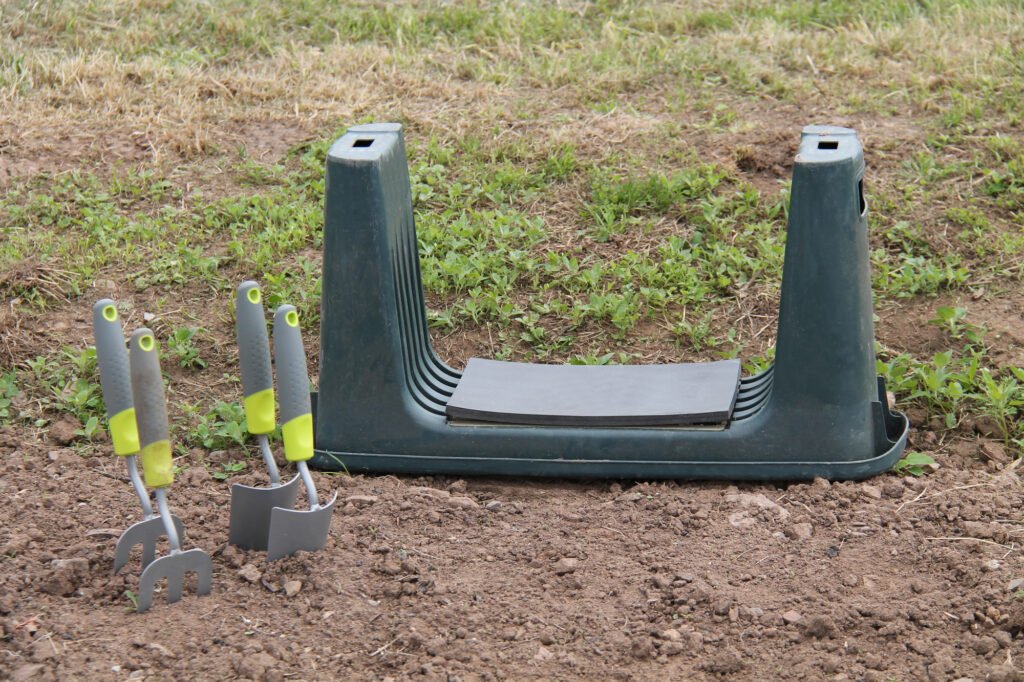Reversible garden kneeler and seat combo beside four ergonomic trowels in mid-day garden.