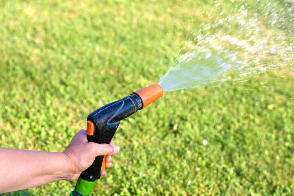 A left hand holds and sprays a lawn with an ergnomic front trigger hose nozzle.
