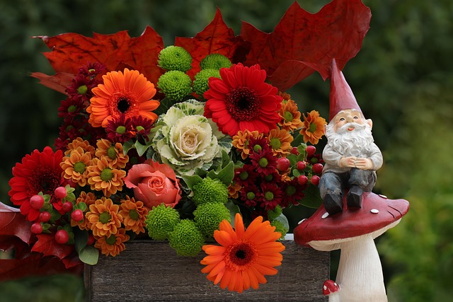 Vibrant autumn flower arrangement with older white bearded gnome sitting beside the arrangement on a red capped mushroom.