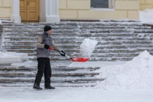 A man clearing snow and ice from outdoor steps during a winter snowstorm.