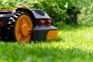 closeup right-side view of robotic lawnmower with black body housing, yellow wheel rims, and red knobs operating on plush lawn during summer afternoon